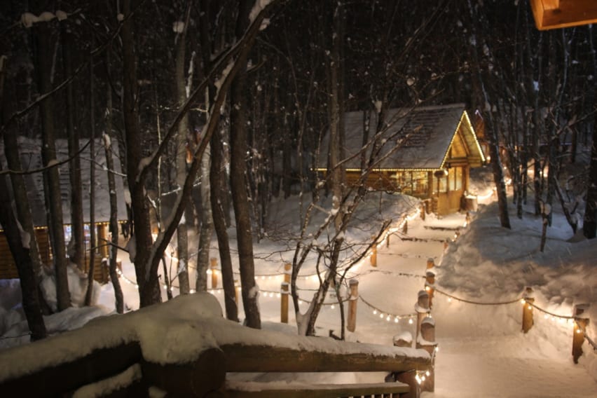 Snow-covered path at Ningle Terrace - The line of illuminated log cabins gives this place a cozy atmosphere